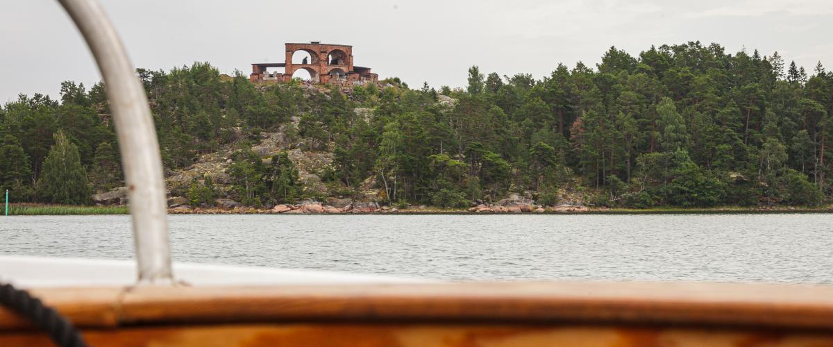 Personen som har tagit bilden sitter i en båt. I förgrunden syns insidan av båten. I bakgrunden ett torn uppe på ett berg som det växer skog på. Mellan båten och berget är det vatten.