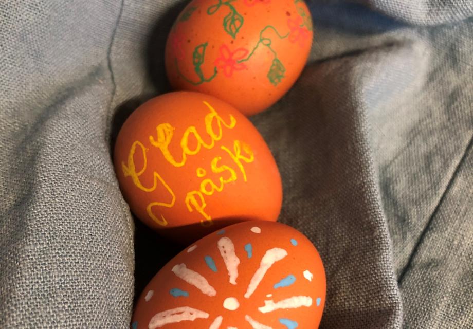 Tre bruna hönsägg som är färggrant dekorerade. På det i mitten står det "Glad påsk"