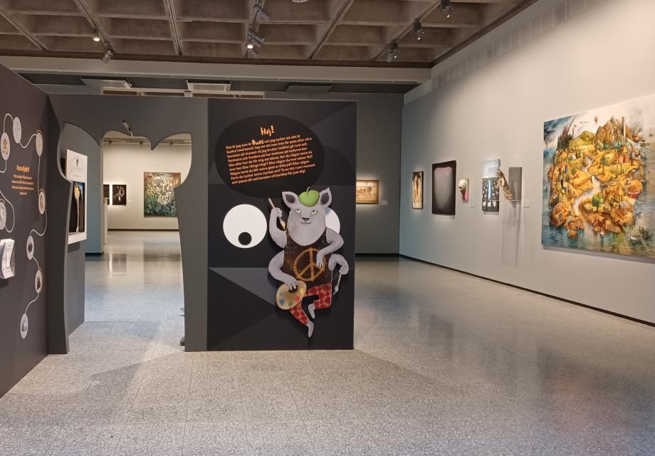 visar en vy över basutställningen med en bild på konstmuseets maskot Busis och olika konstverk i bakgrunden 