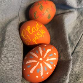 Tre bruna hönsägg som är färggrant dekorerade. På det i mitten står det "Glad påsk"