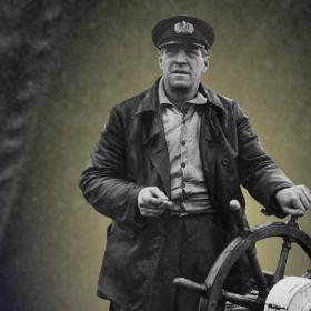 Till höger ett svartvitt foto på Algot Niska i rodret, med kaptenshatt i huvudet och tobak i handen. Bakgrunden är ett otydligt foto på grovt, mörkt tyg. En gul ljusstråle belyser Niskas bakgrund och texten Smugglare och förbudstiden som kastar en skugga och försvinner bortifrån ljuset.