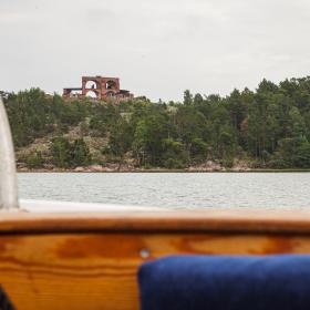 Personen som har tagit bilden sitter i en båt. I förgrunden syns insidan av båten. I bakgrunden ett torn uppe på ett berg som det växer skog på. Mellan båten och berget är det vatten.