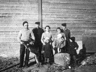 De första fyrvaktarna med sina familjer framför det nybyggda bostadshuset vid 1930-talets slut. Från vänster Volmar Karlsson, radiofyrmästaren Erik Jansson och hans fru Ingrid med sonen Svante, Anni och Valter Finnerman med barnet Gunvor ståendes på stenen. Barnet längst till höger är okänt. (Foto: Ålands landskapsarkiv)