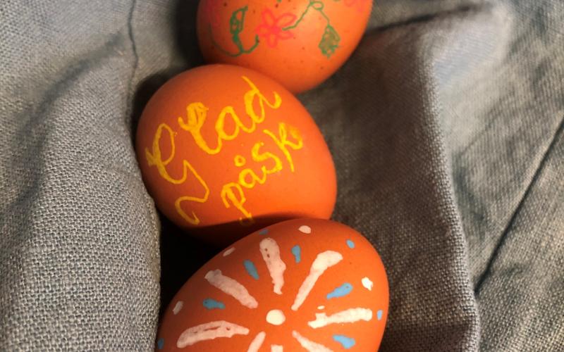 Tre bruna hönsägg som är dekorerade i glada färger. På ägget i mitten står det "Glad påsk",